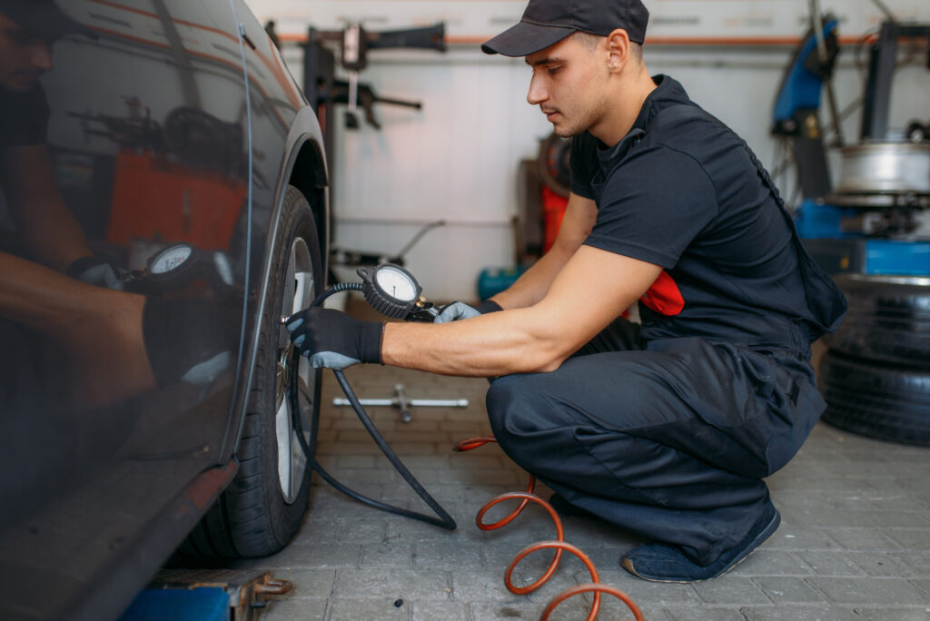 Auto mechanic checks the tire pressure in repairing service. Man repairs car tyre in garage, professional automobile inspection in workshop