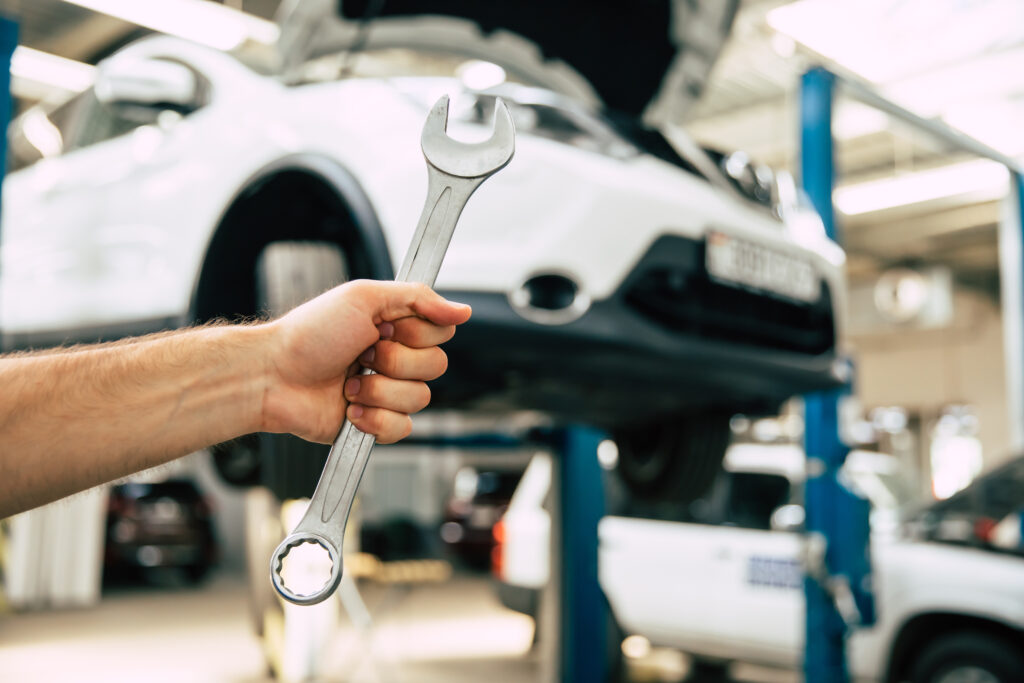 Close up photo of a male auto mechanics hand with an open-end wrench on the background of repairing a car
